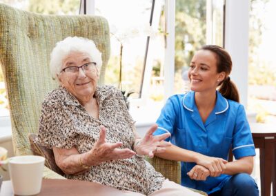 A nurse is talking to an elderly woman in a chair.