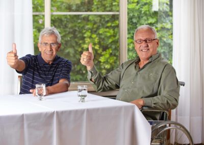 Two men in wheelchairs giving thumbs up at a table.