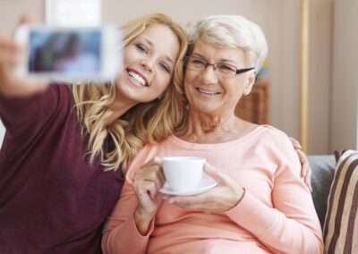 A woman is taking a picture of her grandmother with a cell phone.