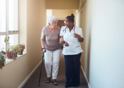 A nurse and an elderly woman walking down a hallway.