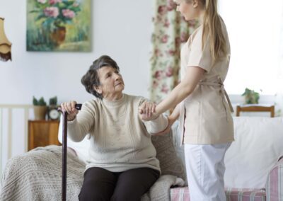 A nurse is helping an elderly woman with a cane.